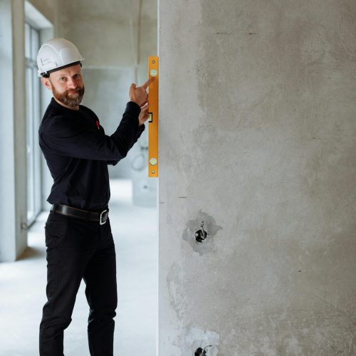 Smiling construction worker using spirit level on concrete wall at a building site.